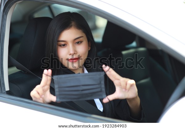 Young asian healthy woman in business\
black suit wearing protect mask for healthcare in automobile and\
driving car. New normal and social distancing\
concept