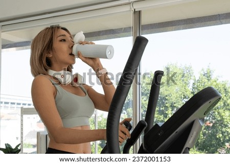 Young Asian Healthy Woman Drinking Water After Workout with Elliptical Machine at Home