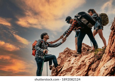 Young Asian Hikers Climbing Up On The Peak Of Mountains. People Helping Each Other Hike Up A Mountain At Sunrise. Giving A Helping Hand. Climbing ,Helps And Team Work Concept.