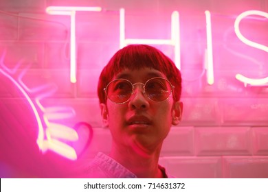 Young Asian Hipster Millennials Man In Street Style Fashion Concept And Wearing Sunglasses In Pink Neon Light