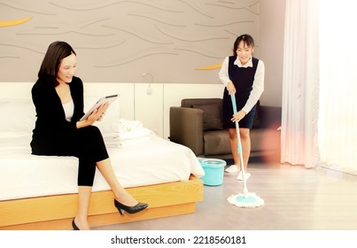 Young Asian Housewife Manager Takes Care Of The Tidiness Cleanliness Training Of The Room Assess The Performance Of The Maid During Service Work Between The Female Worker Cleaning The Floor With Mop.