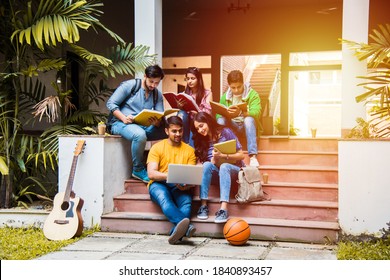 Young Asian Indian College Students Reading Books, Studying On Laptop, Preparing For Exam Or Working On Group Project While Sitting On Grass, Staircase Or Steps Of College Campus