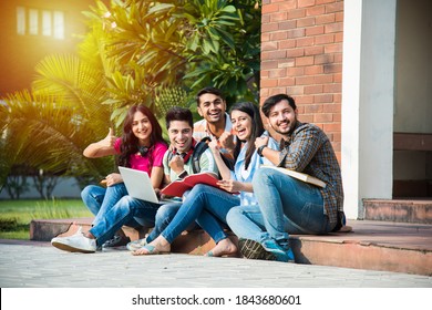 Young Asian Indian college students reading books, studying on laptop, preparing for exam or working on group project while sitting on grass, staircase or steps of college campus
