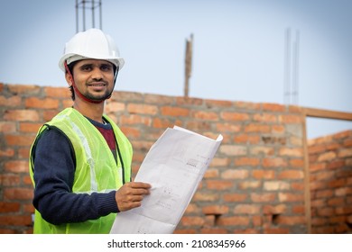 young Asian Indian Engineer holding drawing layout blueprint looking on camera.