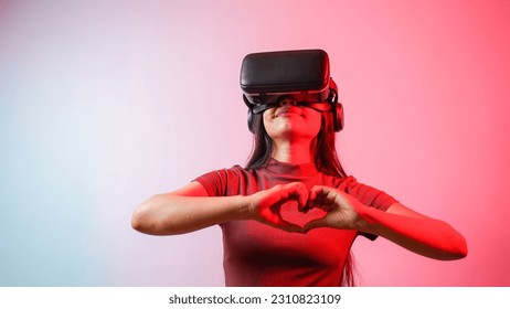 Young Asian Indian woman holding heart-shaped hands, wearing virtual reality headset, a girl with vr glasses concept studio portrait - Powered by Shutterstock