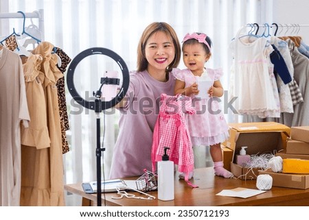 Young Asian influencer mother is selling the children clothes live online streaming at home while raising her toddler as assistance [[stock_photo]] © 