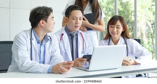 Young Asian Intern, Young Male And Female Doctor Sitting With Senior Doctor Talk And Discuss Using Laptop In Office.