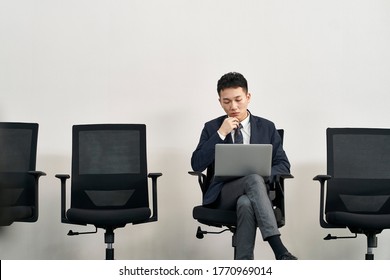 Young Asian Job Seeker Sitting In Chair Preparing For Interview Using Laptop Computer While Waiting In Line