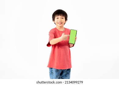 Young Asian Kid Holding A Phone In His Hands With A Green Screen Standing On A White Isolated Background With Copy Space.