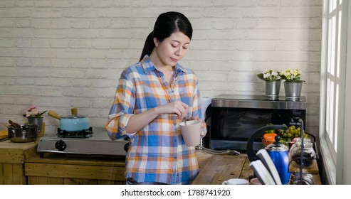 Young asian korean female stir cup of coffee in morning at home kitchen. elegant girl smiling preparing drink for breakfast. relax lady mixing sugar into mug while standing against window indoors - Powered by Shutterstock