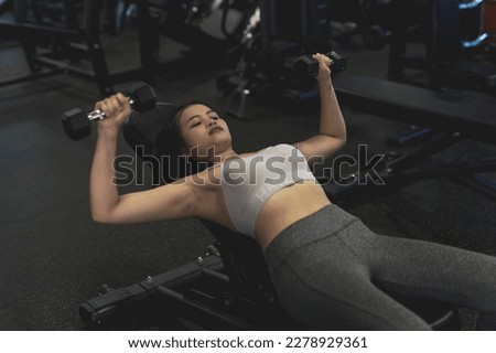 A young asian lady does a set of incline dumbbell presses. Training chest at the gym.