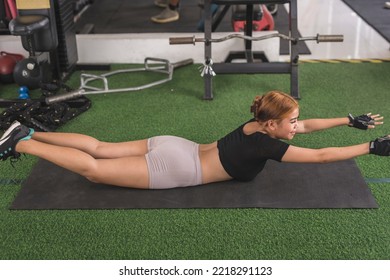 A Young Asian Lady Does Superman Back Extensions On A Black Mat. Isometric Exercise. Working Out And Training Lower Back Muscles At A Home Gym.