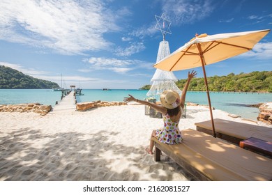 Young Asian lady tourist sitting on the wooden chaise longue in to the sea on her holiday.