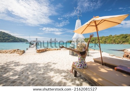 Young Asian lady tourist sitting on the wooden chaise longue in to the sea on her holiday.