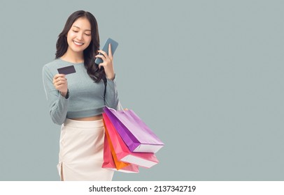 Young asian lady using mobile phone holding credit card carry shopping bags isolated over pastel green background and copy space Smiling young girl purchasing online through phone using credit card - Shutterstock ID 2137342719