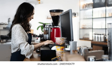 Young asian lady waitress using computer desktop for payment in coffee shop counter. beautiful woman staff enter customer order from note into point of sale terminal machine in cafe store. - Powered by Shutterstock