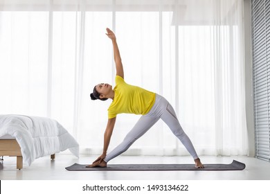 Young Asian Lady Wearing Yellow T Shirt Doing Exercise Yoga Pose In The Bedroom In The Morning After Woke Up.