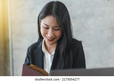 Young Asian Lawyer Woman Professional In A Suit Sitting At A Desk In Her Office. She Looks, Happy, Hopeful And Confident About Her Future.