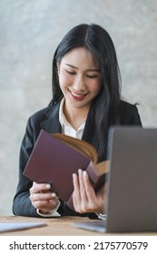 Young Asian Lawyer Woman Professional In A Suit Sitting At A Desk In Her Office. She Looks, Happy, Hopeful And Confident About Her Future.