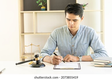 Young Asian Lawyer Working On Financial Audit And Client Support While Working Hard In The Office. Delegate Legal Concept Litigation With Hammers And Scales Placed In Front Of You.