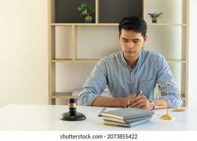 Young Asian Lawyer Working On Financial Audit And Client Support While Working Hard In The Office. Delegate Legal Concept Litigation With Hammers And Scales Placed In Front Of You.