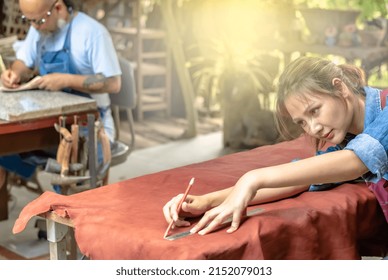 Young Asian Leather Maker Woman Using Pencil And Ruler Measure To Draw A Large Leather Pattern On Work Table With Male Leather Specialist Working On The Side In Leather Workshop, Busy Working Woman 