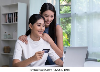 Young Asian Lesbian Couple Holding Credit Card And Using Laptop Computer. LGBT Lesbian Businesswoman Working At Home. Online Shopping, E-commerce, Internet Banking, Spending Money, Working From Home.