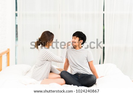 Young Asian lovely couple flirting together on bed in white bedroom. Girlfriend and boyfriend teasing each other. Love, Valentine's day happiness activity, wedding people, or students dating concept