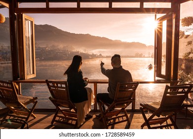 Young asian lover couple sitting on chair at a little cafe, Drinking coffee look at Sunrise in morning view mist and riverside view, Chinese settlement, Lee wine Rak Thai, Mae Hong Son, Thailand.