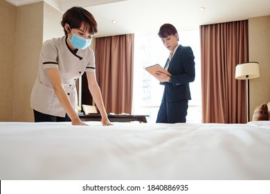 Young Asian Maid Wearing Medical Mask When Making Bed In Hotel Room Under Control Of Manager