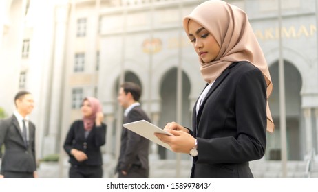 Young Asian Malay Girl Wearing Suit Holding Tablet Computer At Office Building