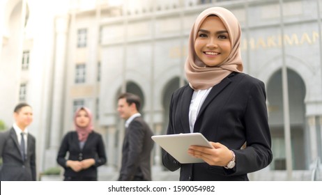 Young Asian Malay Girl Wearing Suit Holding Tablet Computer And Smile To The Camera