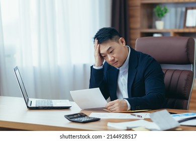 Young Asian Male Accountant, Office Worker Working With Documents, Tired, Sitting At Desk In Office