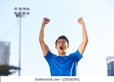 Young Asian Male Athlete Celebrating Victory With Fists And Arms Raised