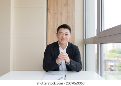 Young Asian Male Businessman Talking Online On Video Call, Conference Or Meeting Looking At Camera. Webcam View. Asia Man In Business Suit Indoors. Office Negotiations Distance Consultation Or Advice