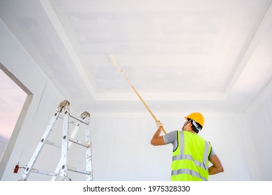 Young Asian Male Construction Worker Work As A House Painter Painting The Ceiling Inside The House And Using A White Primer Paint Roller On The Construction Site.