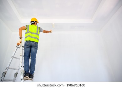 Young Asian Male Construction Worker Work As A House Painter Painting The Ceiling Inside The House And Using A White Primer Paint Roller On The Construction Site.