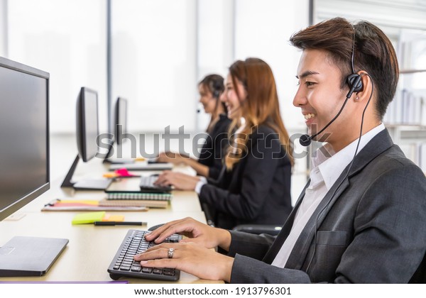 Young\
Asian male customer service support agent operator team working in\
call center office with headsets and\
computer.