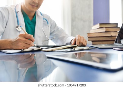 Young Asian Male Doctor Is Working With Laptop And Digital Tablet In A Medical Room At A Hospital.