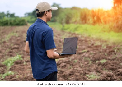 A young Asian male farmer uses a laptop to analyze, evaluate and trade his cash crops. - Powered by Shutterstock