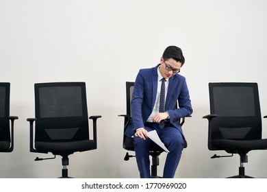 Young Asian Male Job Seeker Sitting In Chair With Head Down Appears To Be Frustrated And Defeated