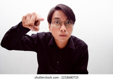 Young Asian Male Millenial Worker Or Student Wearing Black Tshirt Isolated Over White Background Angry, Mad, Frustrated. Man Pointing To Camera Angrily.