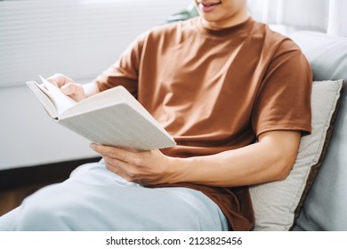 Young Asian Male Reading A Book In Sofa Relaxation At Home Concept.