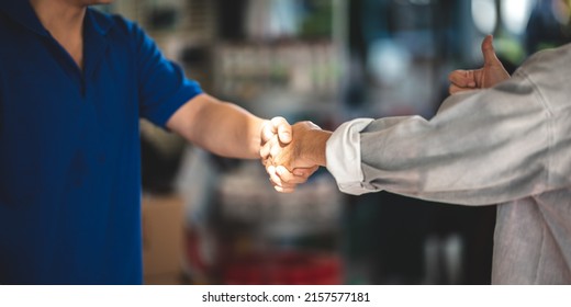 Young Asian male smiling car mechanic shaking hands with senior customer wearing spectacles and showing thumbs up gesture while standing in garage on a bright sunny day - Powered by Shutterstock