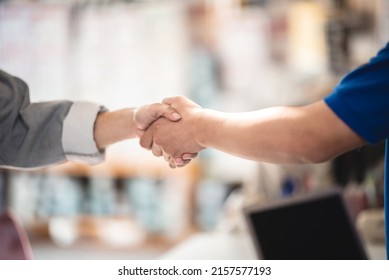 Young Asian male smiling car mechanic shaking hands with senior customer wearing spectacles and showing thumbs up gesture while standing in garage on a bright sunny day - Powered by Shutterstock