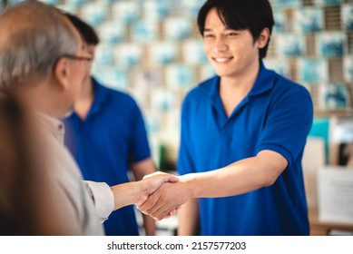 Young Asian male smiling car mechanic shaking hands with senior customer wearing spectacles and showing thumbs up gesture while standing in garage on a bright sunny day - Powered by Shutterstock