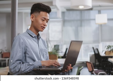 Young Asian male student using his laptop, copy space. Casual businessman typing on his computer, working at the office. Male entrepreneur working on a project online - Shutterstock ID 1369348598