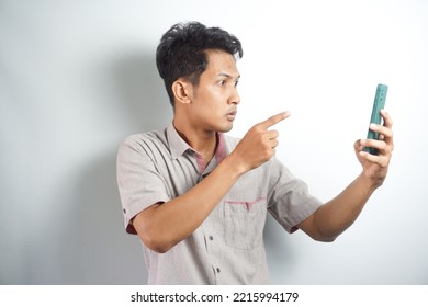 Young Asian Man Angry, Frustrated And Furious With His Phone, Angry With Customer Service Over White Background.