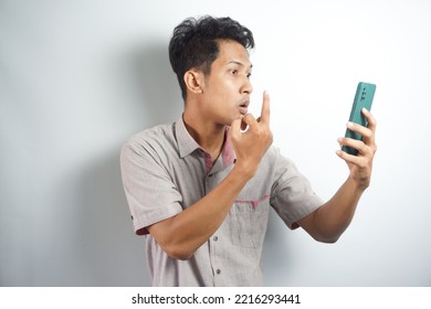 Young Asian Man Angry, Frustrated And Furious With His Phone, Angry With Customer Service Over White Background.