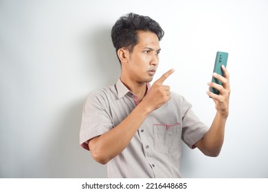 Young Asian Man Angry, Frustrated And Furious With His Phone, Angry With Customer Service Over White Background.